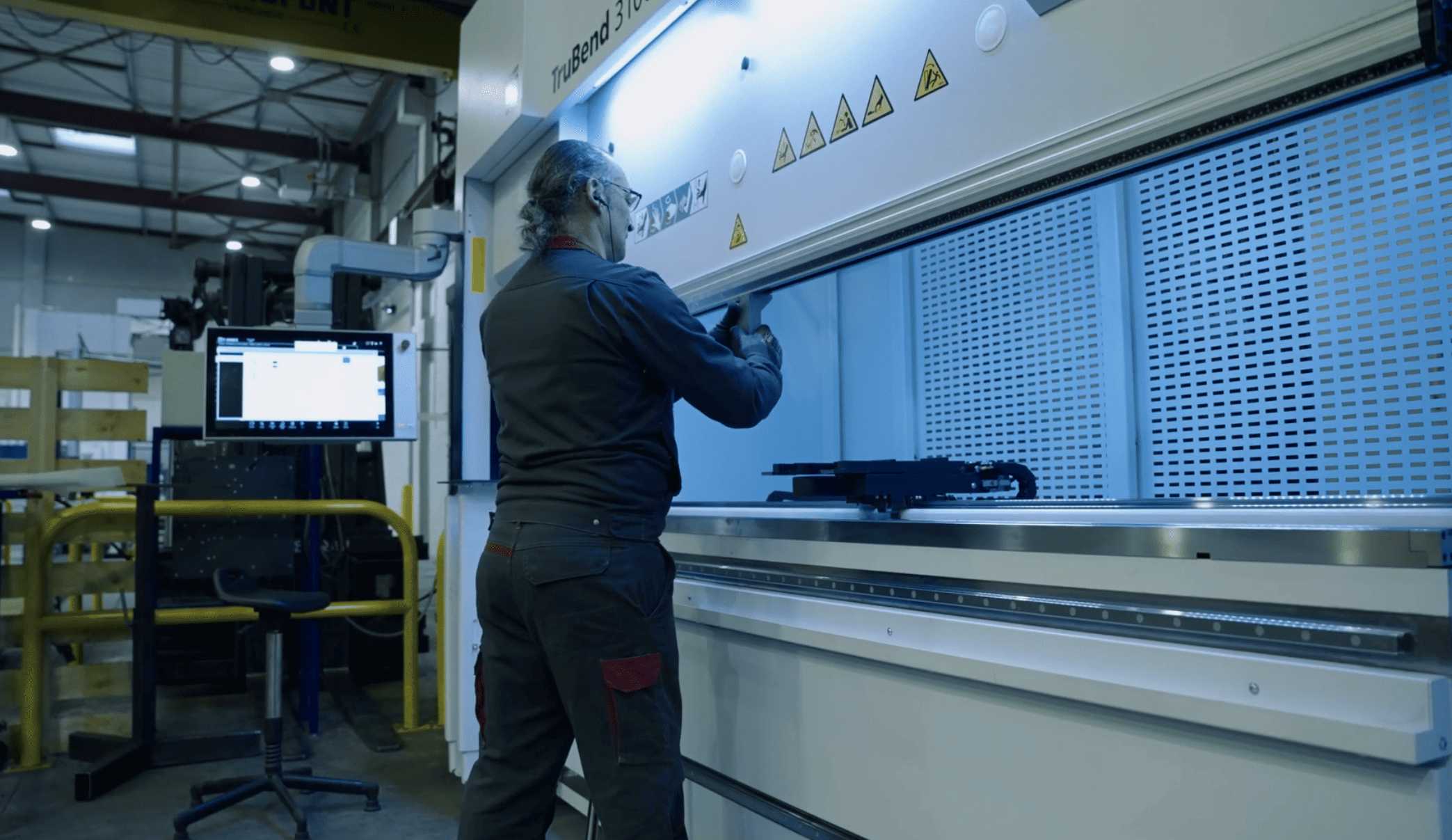 Opérateur au travail sur une plieuse industrielle, atelier en lumière bleutée